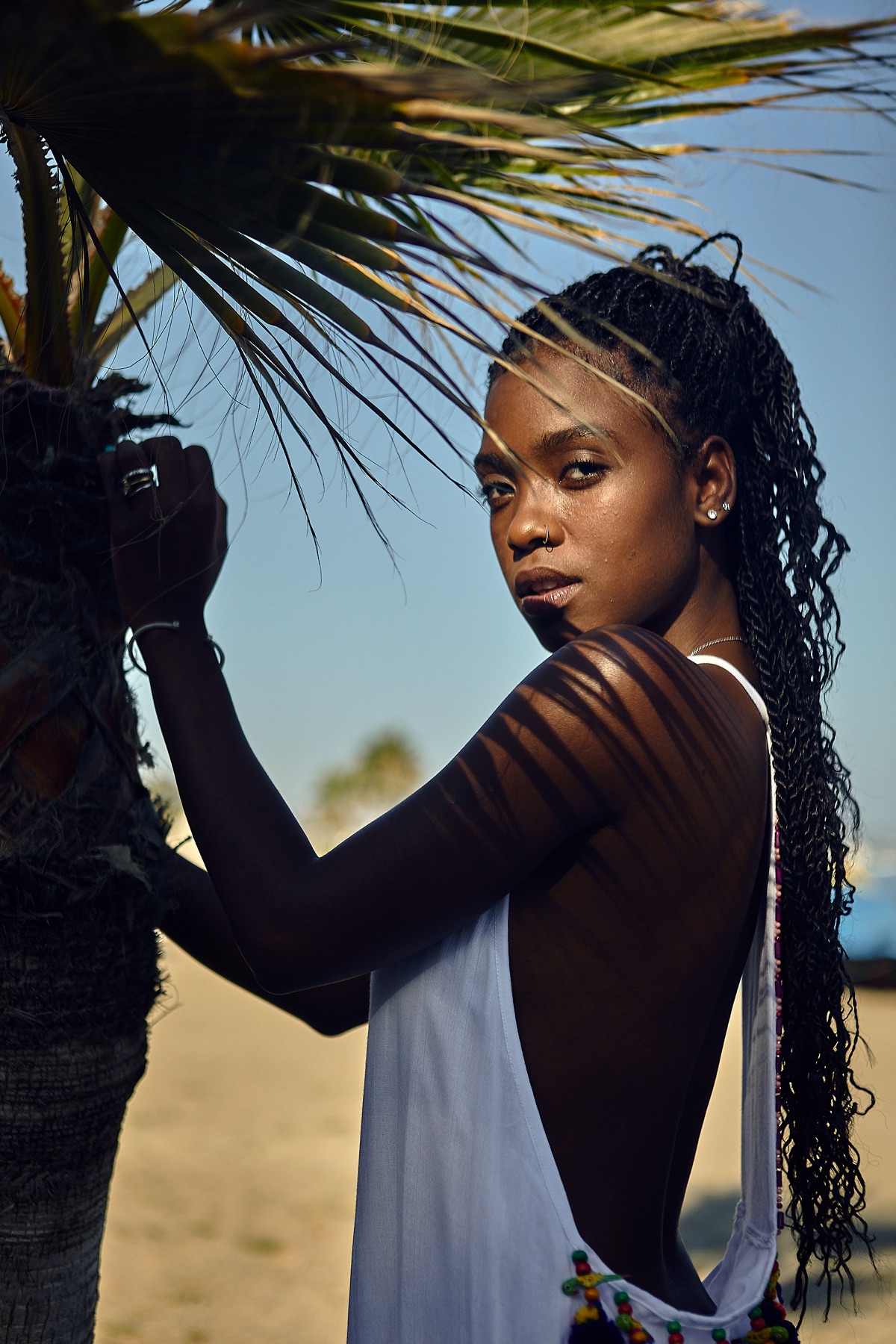 Retrato de moda junto a una palmera, con luz natural y sombras sobre el hombro